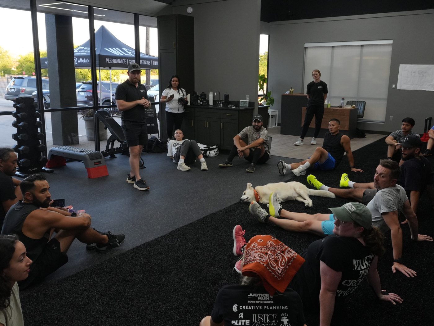 A group session on the floor at WLF Club, fifteen people stretching while a coach talks them through it.