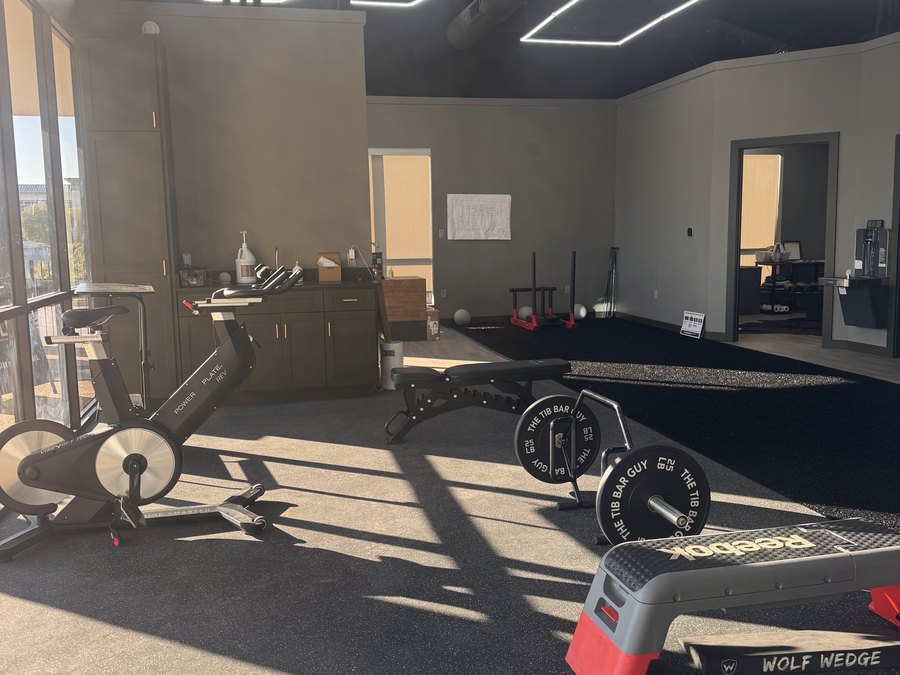 The gym floor at WLF Club in late afternoon light, with an assault bike, benches, and a turf lane.