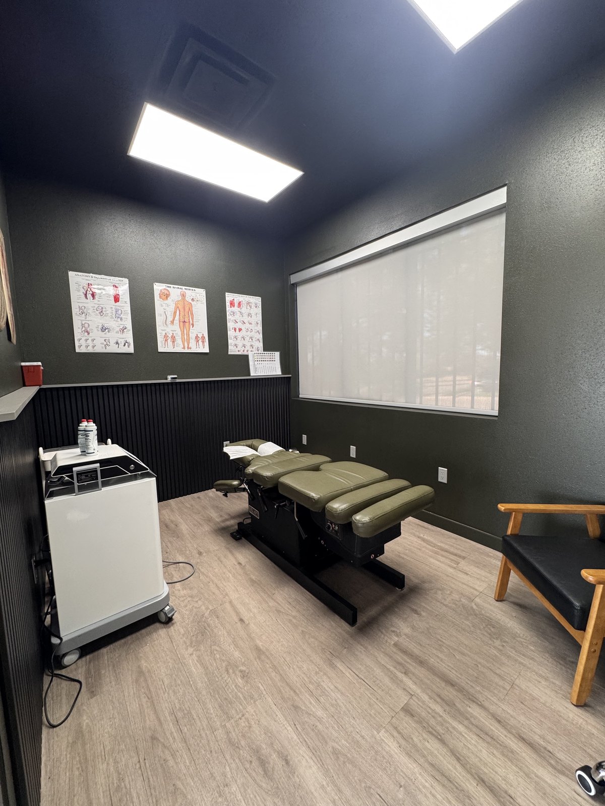 A treatment room at WLF Club with an adjustment table, a rolling therapy cart, and anatomy charts on the wall.